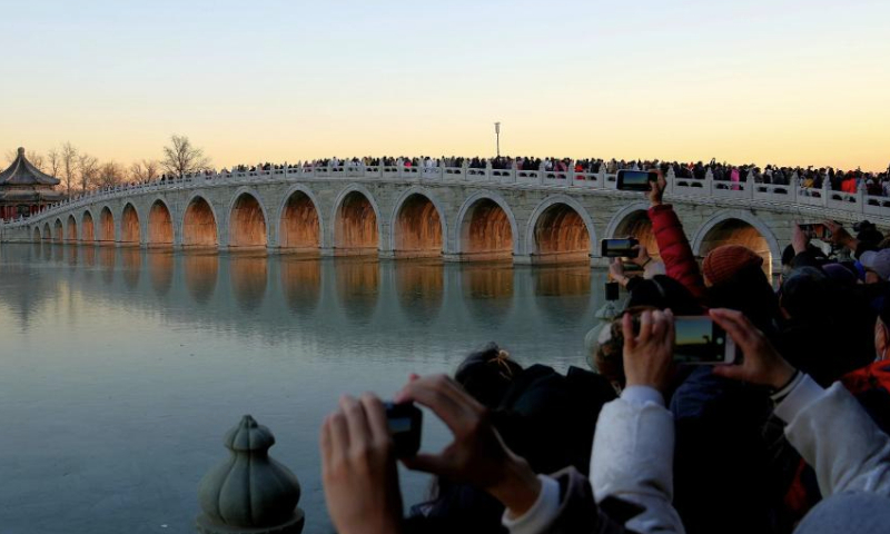 Visitors take photos of the illuminated 17-Arch Bridge at sunset in the Summer Palace in Beijing, capital of China on Dec. 22, 2024. (Xinhua/Xing Guangli)