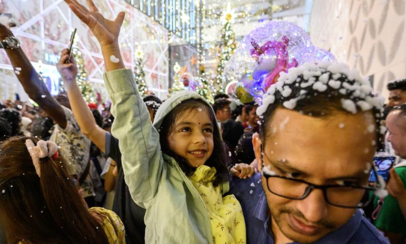 People are seen with artificial snowflakes on a street in Kuala Lumpur, Malaysia, Dec. 22, 2024. (Photo by Chong Voon Chung/Xinhua)