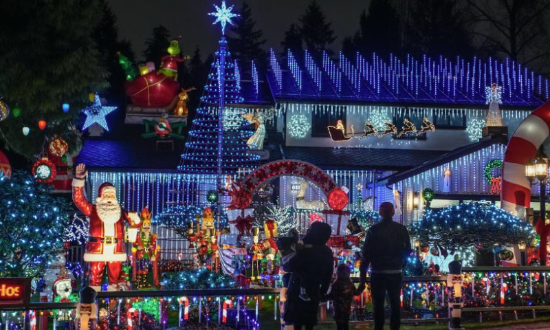 People are pictured in front of a residential house adorned with Christmas lights and decorations on a street in Vancouver, British Columbia, Canada, Dec. 22, 2024. (Photo by Liang Sen/Xinhua)