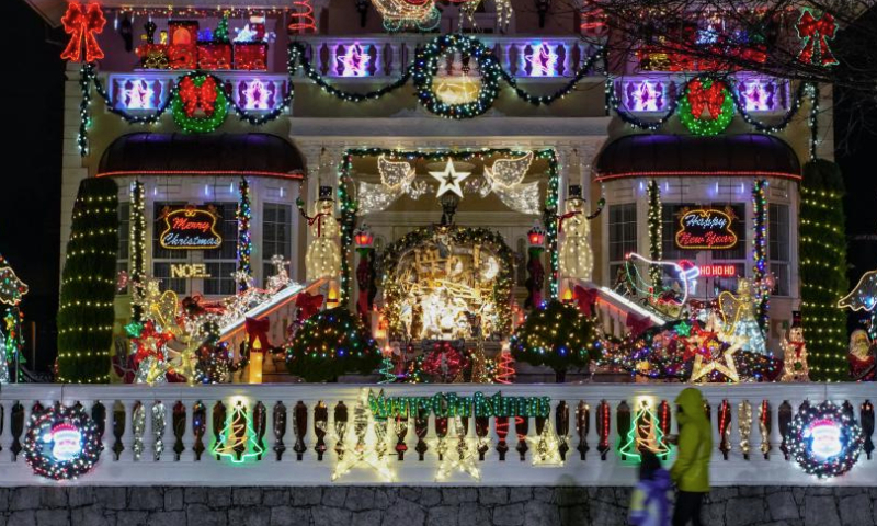 People walk past a residential house adorned with Christmas lights and decorations on a street in Vancouver, British Columbia, Canada, Dec. 22, 2024. (Photo by Liang Sen/Xinhua)