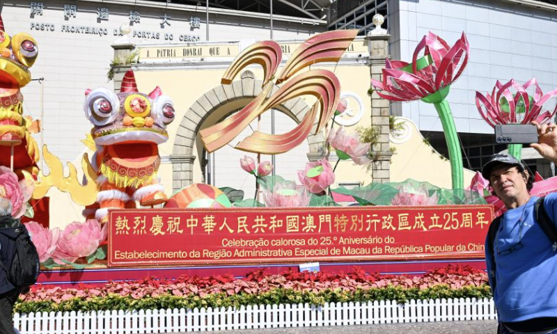 A tourist takes selfies in front of a celebration installation at the Border Gate in Macao, south China, Dec. 18, 2024. The streets of Macao have been adorned by festive decorations, as the city is set to mark the 25th anniversary of its return to the motherland. (Xinhua/Cheng Yiheng)