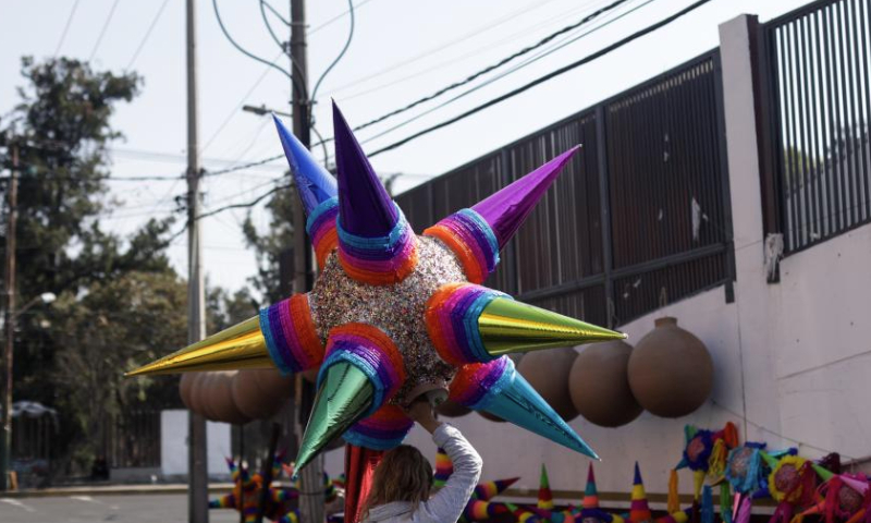 A woman carries a pinata in Mexico City, Mexico, Dec. 13, 2024. Pinata, traditionally crafted in the shape of a seven-pointed star, is filled with candies and small gifts, bringing joy and festive spirit to celebrations. (Xinhua/Francisco Canedo)