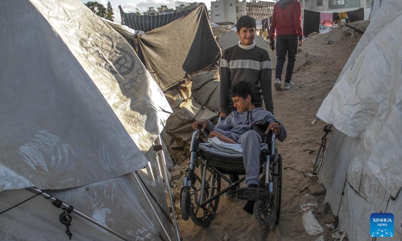 A boy helps push the wheelchair for Akram Harb (front) in Gaza City, on Dec. 13, 2024. Harb, a 13-year-old Palestinian, was injured in an Israeli attack at his house in the Jabalia refugee camp in the northern Gaza Strip in October, 2024. (Photo: Xinhua)