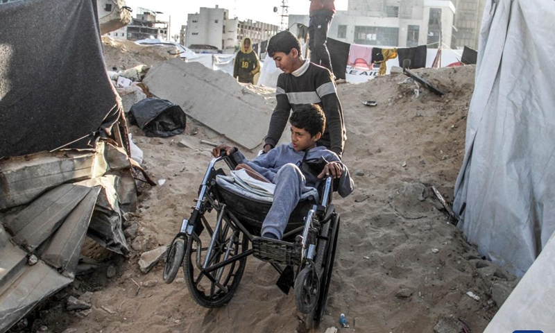 A boy helps push the wheelchair for Akram Harb (front) in Gaza City, on Dec. 13, 2024. Harb, a 13-year-old Palestinian, was injured in an Israeli attack at his house in the Jabalia refugee camp in the northern Gaza Strip in October, 2024. (Photo: Xinhua)