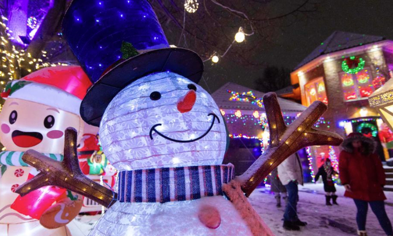 People look at colorful lights and decorations outside a residential house in Mississauga, Ontario, Canada, on Dec. 23, 2024. (Photo by Zou Zheng/Xinhua)