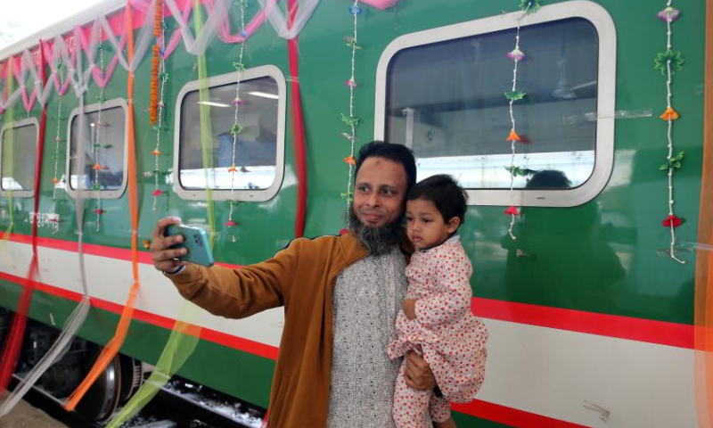 A man takes selfies with his child in front of the first train of the Padma Bridge Rail Link Project (PBRLP) at Dhaka station, Dhaka, Bangladesh, Dec. 24, 2024. With the first train decorated with colorful ribbons arriving at Dhaka station, Bangladesh's largest railway Padma Bridge Rail Link Project (PBRLP) officially opened across its entire line to traffic here Tuesday. The PBRLP, one of the significant projects under the Belt and Road Initiative (BRI) in Bangladesh, was built by the China Railway Group Limited (CREC) and funded by the Export-Import Bank of China. The railway, known locally as the Dream Road, stretches approximately 170 km. Following its opening, travel time between the capital Dhaka and the southwestern city of Jashore will be reduced from the original 10 hours to just three hours. (Xinhua)