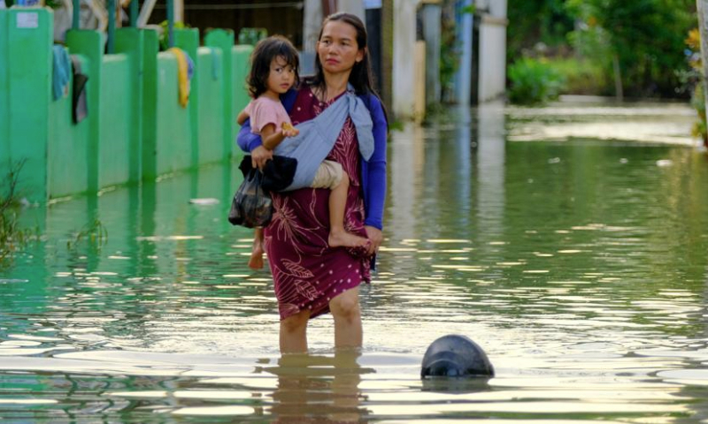 A woman holding a girl walks through flood water after heavy rain hit Makassar, South Sulawesi Province, Indonesia, on Dec. 24, 2024. Floods and landslides have been hitting several regions in the Southeast Asian archipelago in the past week. (Photo by Niaz Sharief/Xinhua)