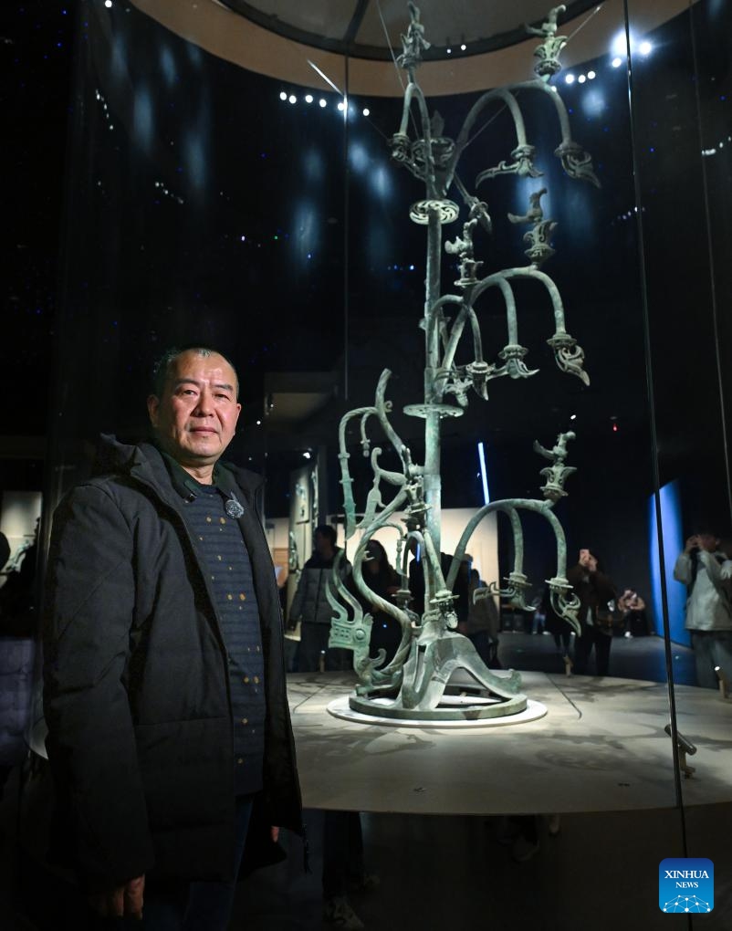 Guo Hanzhong poses for photo with bronze sacred tree at Sanxingdui Museum in Guanghan City, southwest China's Sichuan Province, Dec. 18, 2024.