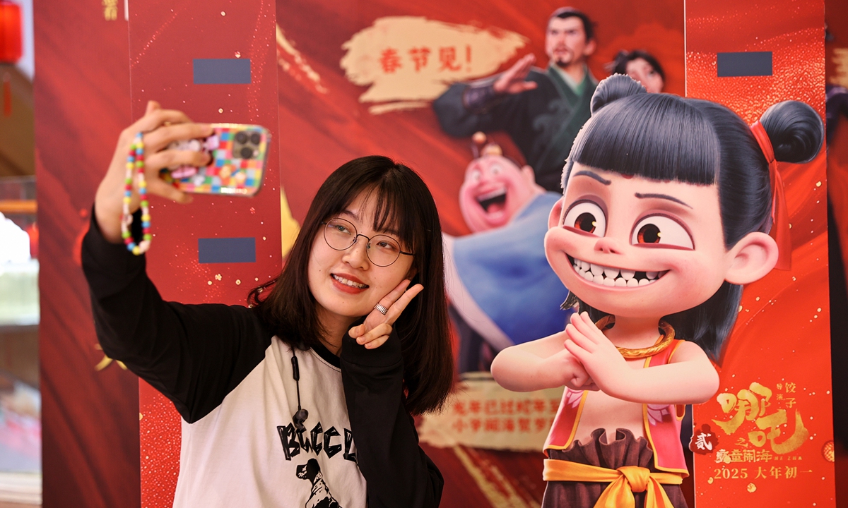 People pose for photos in front of movie posters for <em>Ne Zha 2</em>in Shenyang, Northeast China's Liaoning Province, during a series of cultural activities related to the movie on February 12, 2025. 